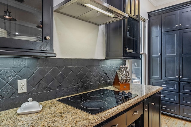 kitchen featuring light stone counters, ornamental molding, wall chimney exhaust hood, black electric stovetop, and tasteful backsplash