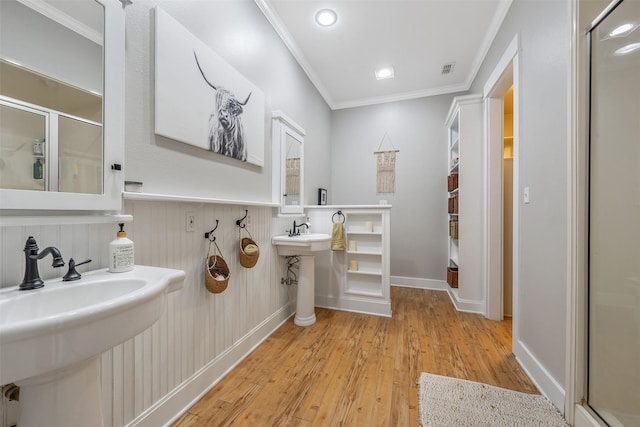 full bath with a sink, ornamental molding, wood finished floors, and a stall shower