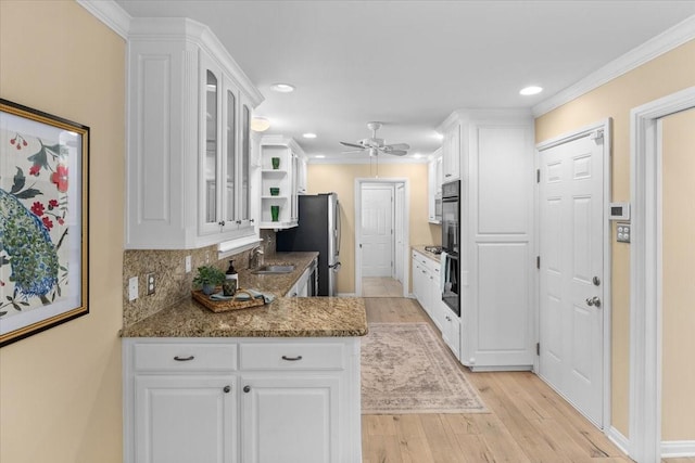 kitchen with a sink, white cabinetry, light wood-style flooring, ceiling fan, and glass insert cabinets