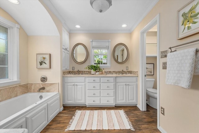 bathroom featuring crown molding, a bath, wood finished floors, toilet, and double vanity