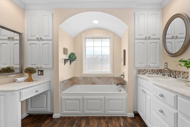 bathroom featuring vanity, a bath, wood finished floors, and tasteful backsplash