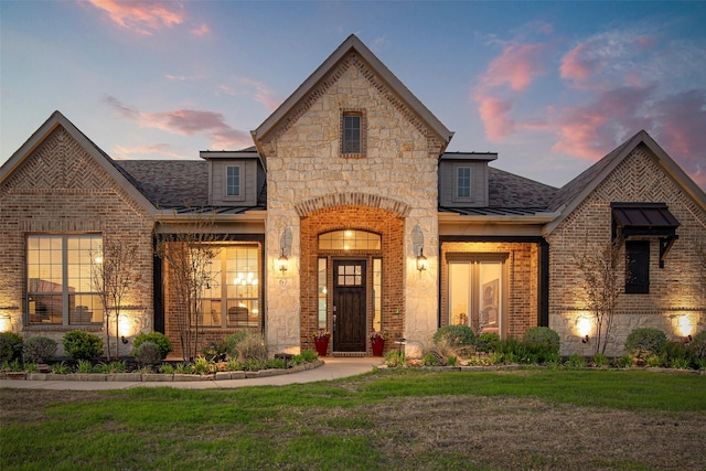 french country inspired facade with brick siding, a front yard, metal roof, and stone siding