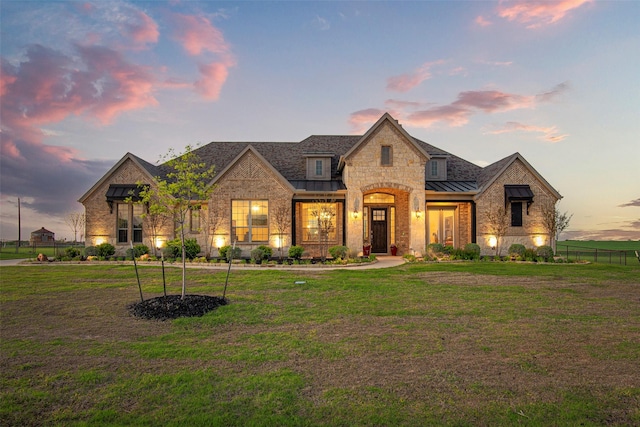 french provincial home featuring a standing seam roof, a front yard, metal roof, and fence