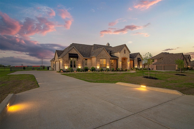 french provincial home featuring a garage, a front yard, fence, stone siding, and driveway