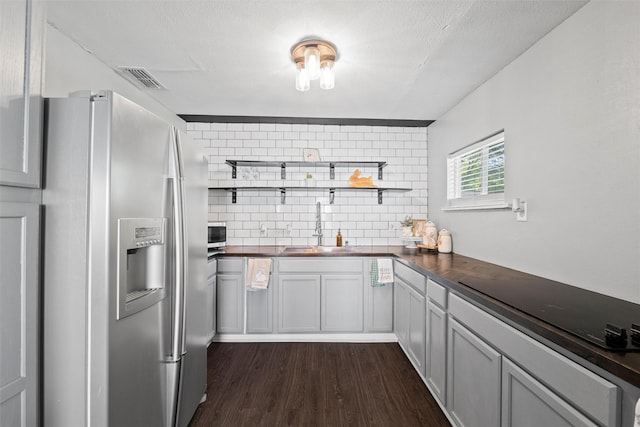 kitchen featuring a sink, open shelves, stainless steel refrigerator with ice dispenser, backsplash, and dark wood finished floors