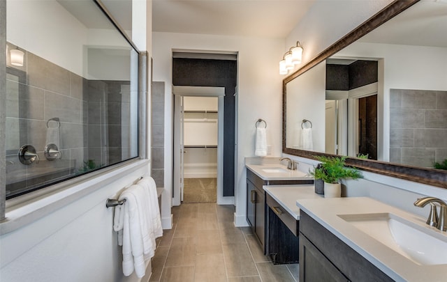 bathroom with two vanities, a sink, a walk in closet, and tiled shower