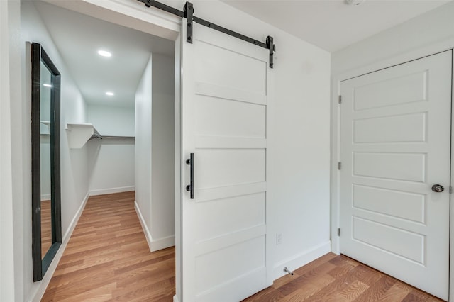 hallway featuring light wood-style flooring, recessed lighting, a barn door, and baseboards