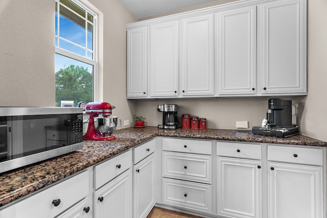 kitchen with stainless steel microwave, white cabinets, and dark stone counters