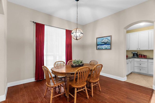 dining area with arched walkways, light wood-style floors, and baseboards