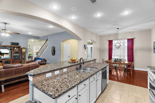 kitchen featuring dishwasher, a sink, arched walkways, white cabinetry, and ceiling fan with notable chandelier