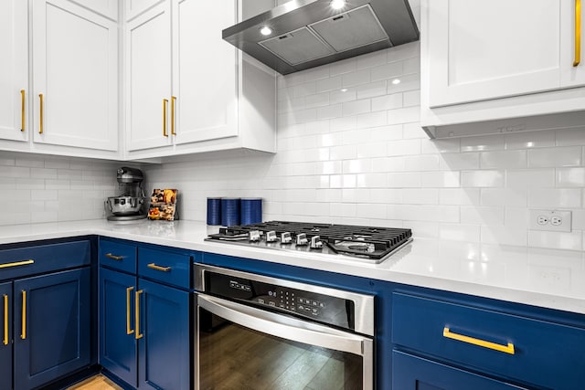 kitchen featuring appliances with stainless steel finishes, decorative backsplash, blue cabinetry, and wall chimney exhaust hood