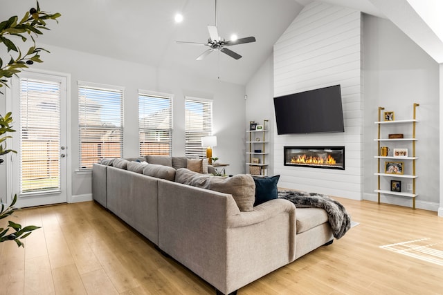 living room featuring light wood-style flooring, ceiling fan, high vaulted ceiling, and a large fireplace