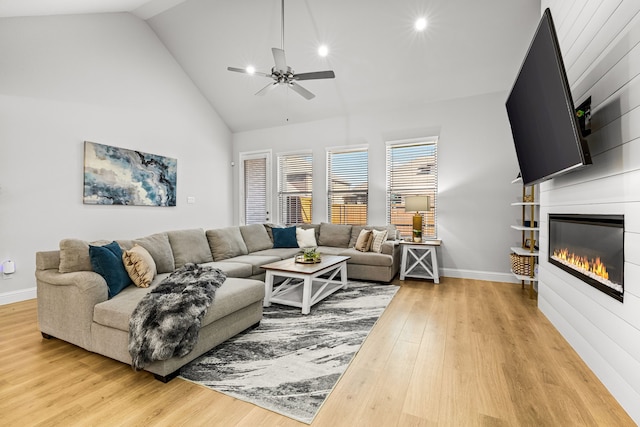 living area featuring ceiling fan, a large fireplace, baseboards, and light wood finished floors