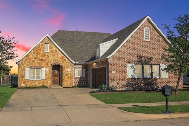 view of front of home with driveway, stone siding, an attached garage, a front lawn, and brick siding