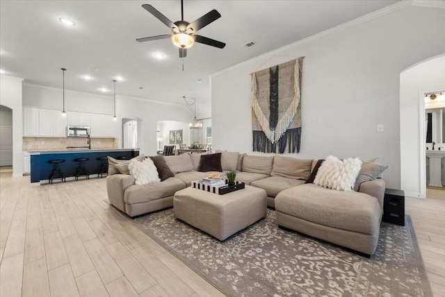living room featuring ceiling fan, arched walkways, ornamental molding, visible vents, and light wood finished floors