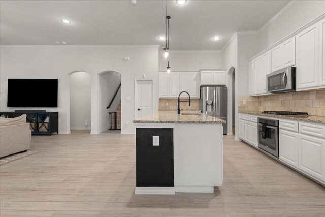 kitchen with stainless steel appliances, arched walkways, crown molding, and light stone counters