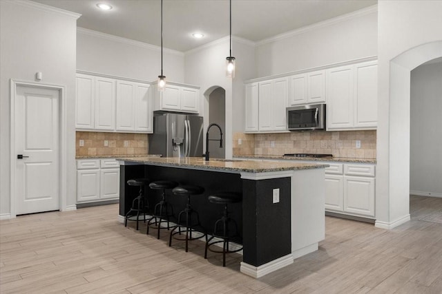 kitchen with tasteful backsplash, arched walkways, a sink, appliances with stainless steel finishes, and a center island with sink