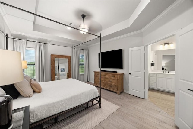 bedroom with light wood-style flooring, ensuite bath, ornamental molding, a sink, and a raised ceiling