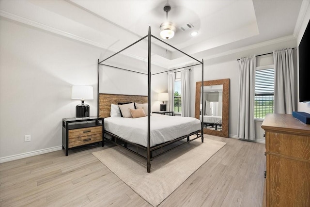 bedroom featuring light wood-style floors, a tray ceiling, ornamental molding, visible vents, and baseboards