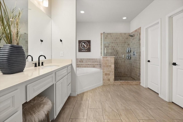 bathroom featuring a bath, a tile shower, recessed lighting, and vanity