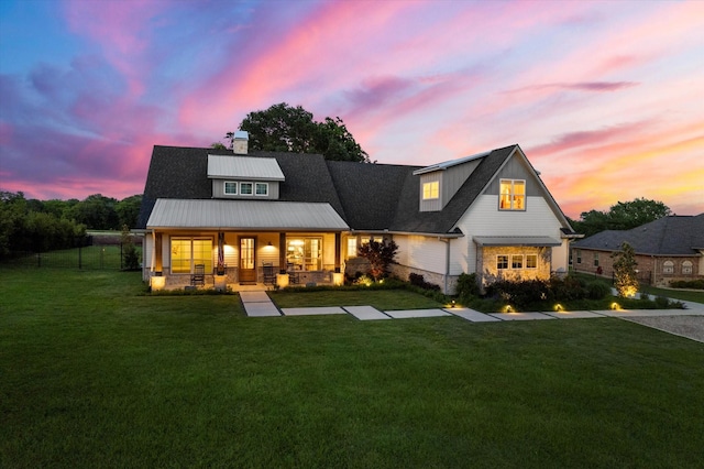 back of property at dusk with a yard, covered porch, and a chimney