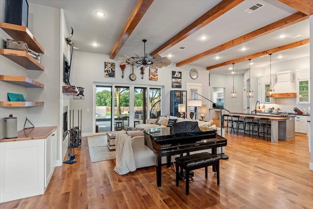 living area featuring visible vents, baseboards, light wood-type flooring, a ceiling fan, and beam ceiling
