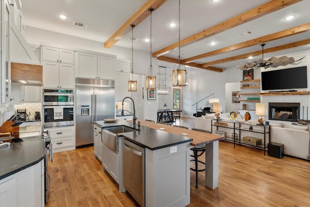 kitchen featuring visible vents, dark countertops, a sink, stainless steel appliances, and open floor plan