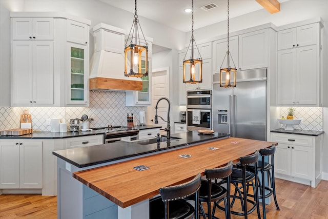 kitchen with visible vents, a center island with sink, appliances with stainless steel finishes, premium range hood, and light wood finished floors