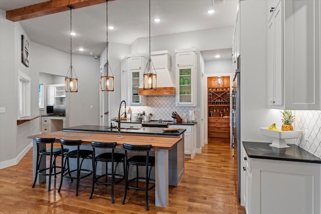 kitchen with custom exhaust hood, a kitchen breakfast bar, an island with sink, white cabinets, and a sink