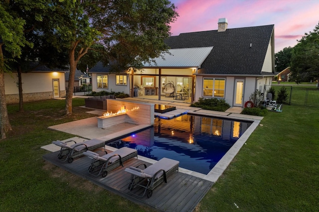 back of property at dusk featuring a yard, fence, a fire pit, a chimney, and a fenced in pool