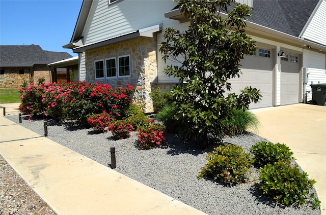 view of side of home with roof with shingles, stone siding, a garage, and concrete driveway