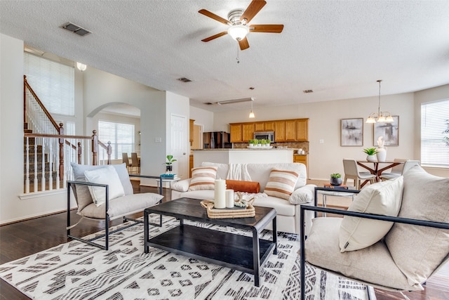 living room with stairs, visible vents, arched walkways, ceiling fan with notable chandelier, and wood finished floors