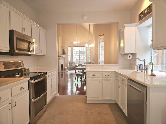 kitchen featuring an inviting chandelier, white cabinetry, appliances with stainless steel finishes, light countertops, and a sink