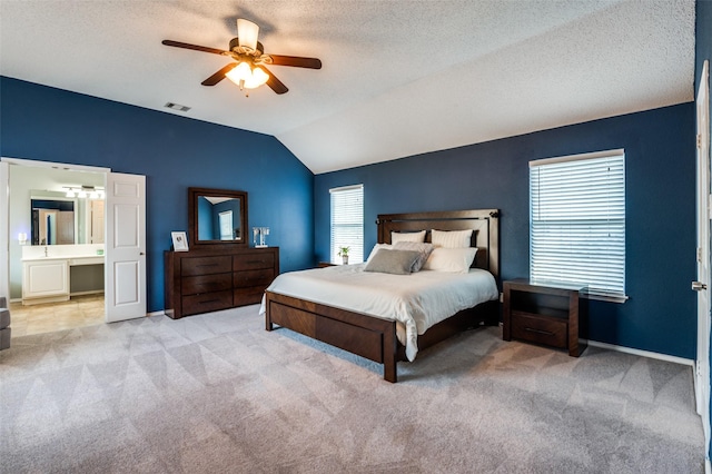 carpeted bedroom featuring lofted ceiling, ceiling fan, baseboards, a textured ceiling, and ensuite bath