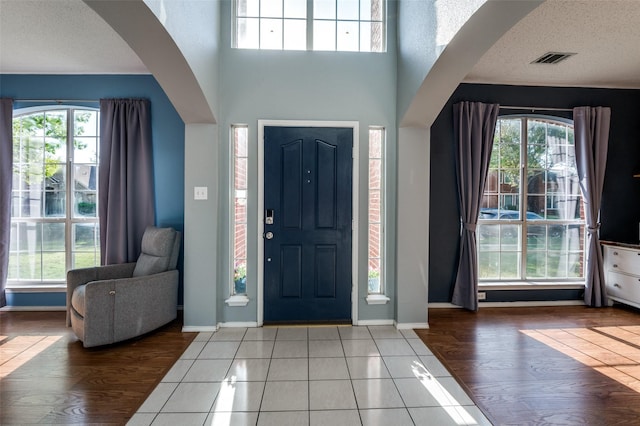 foyer featuring plenty of natural light, arched walkways, baseboards, a towering ceiling, and a textured ceiling