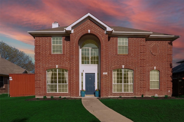 view of front of property with brick siding, a chimney, and a lawn