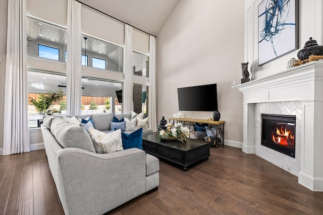 living area with baseboards, high vaulted ceiling, a tile fireplace, and dark wood finished floors