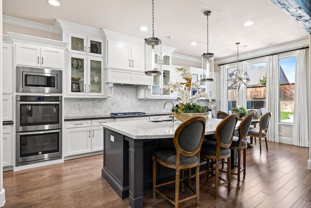 kitchen featuring ornamental molding, appliances with stainless steel finishes, an island with sink, dark wood-style floors, and decorative backsplash