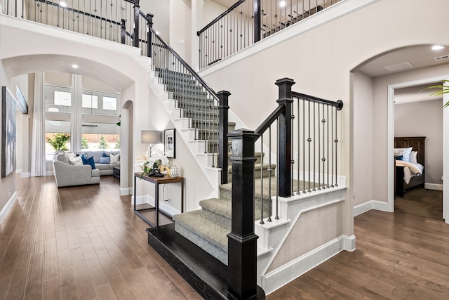 stairway featuring arched walkways, a high ceiling, baseboards, and wood finished floors