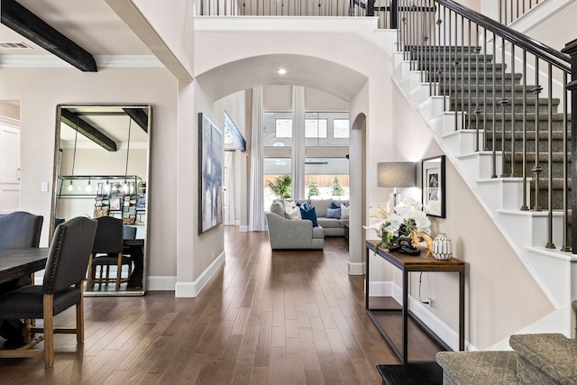 foyer with visible vents, arched walkways, a high ceiling, dark wood-style flooring, and beam ceiling