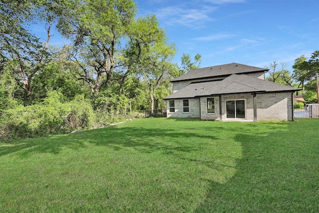 rear view of house with brick siding, fence, a shingled roof, and a lawn