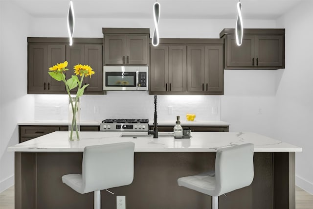 kitchen with an island with sink, light stone countertops, a kitchen bar, appliances with stainless steel finishes, and decorative backsplash