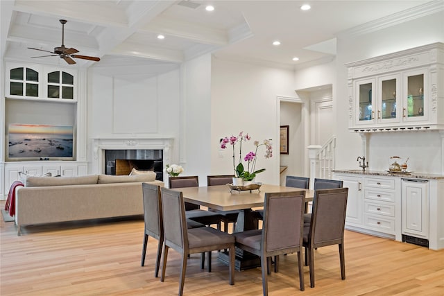 dining room with light wood-type flooring, a ceiling fan, a high end fireplace, crown molding, and beam ceiling