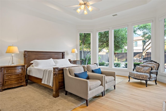 bedroom with a tray ceiling, light wood-style floors, ornamental molding, and visible vents