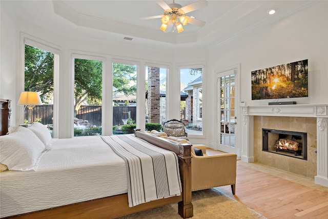 bedroom featuring visible vents, a tiled fireplace, a tray ceiling, access to exterior, and light wood-style flooring