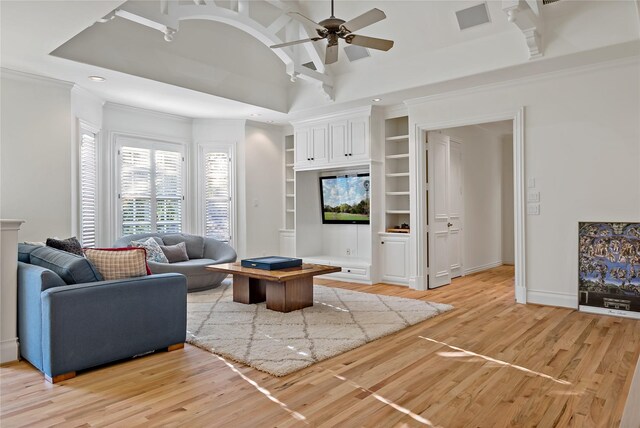 living area featuring built in features, baseboards, ornamental molding, a ceiling fan, and light wood-style flooring