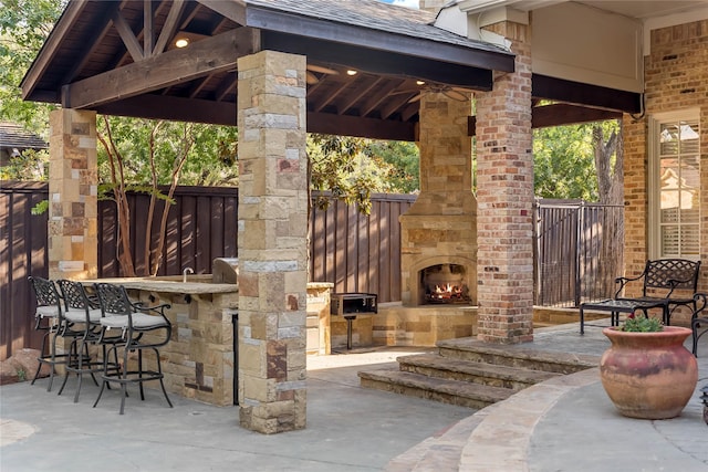 view of patio with a gazebo, an outdoor stone fireplace, fence, and outdoor dry bar