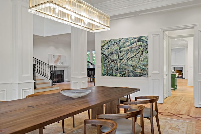 dining space featuring decorative columns, a fireplace, stairway, and light wood finished floors