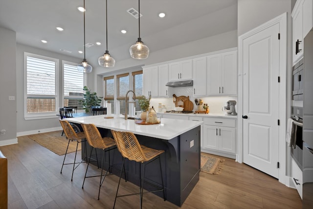 1920 Barnhill Ln, Van Alstyne, TX 75495 - kitchen with a center island with sink, under cabinet range hood, a breakfast bar area, light countertops, and white cabinetry