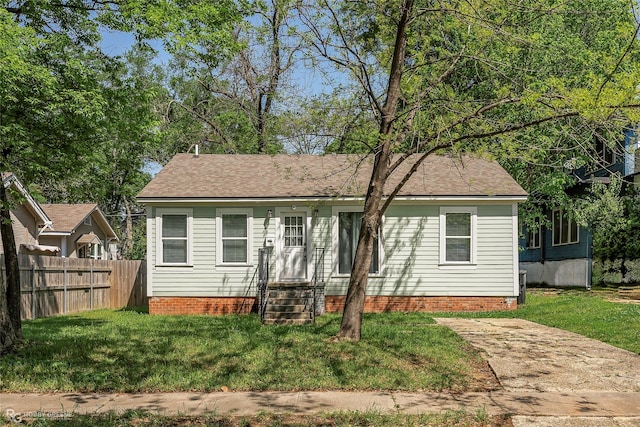 view of front of home with entry steps, a front lawn, fence, and a shingled roof